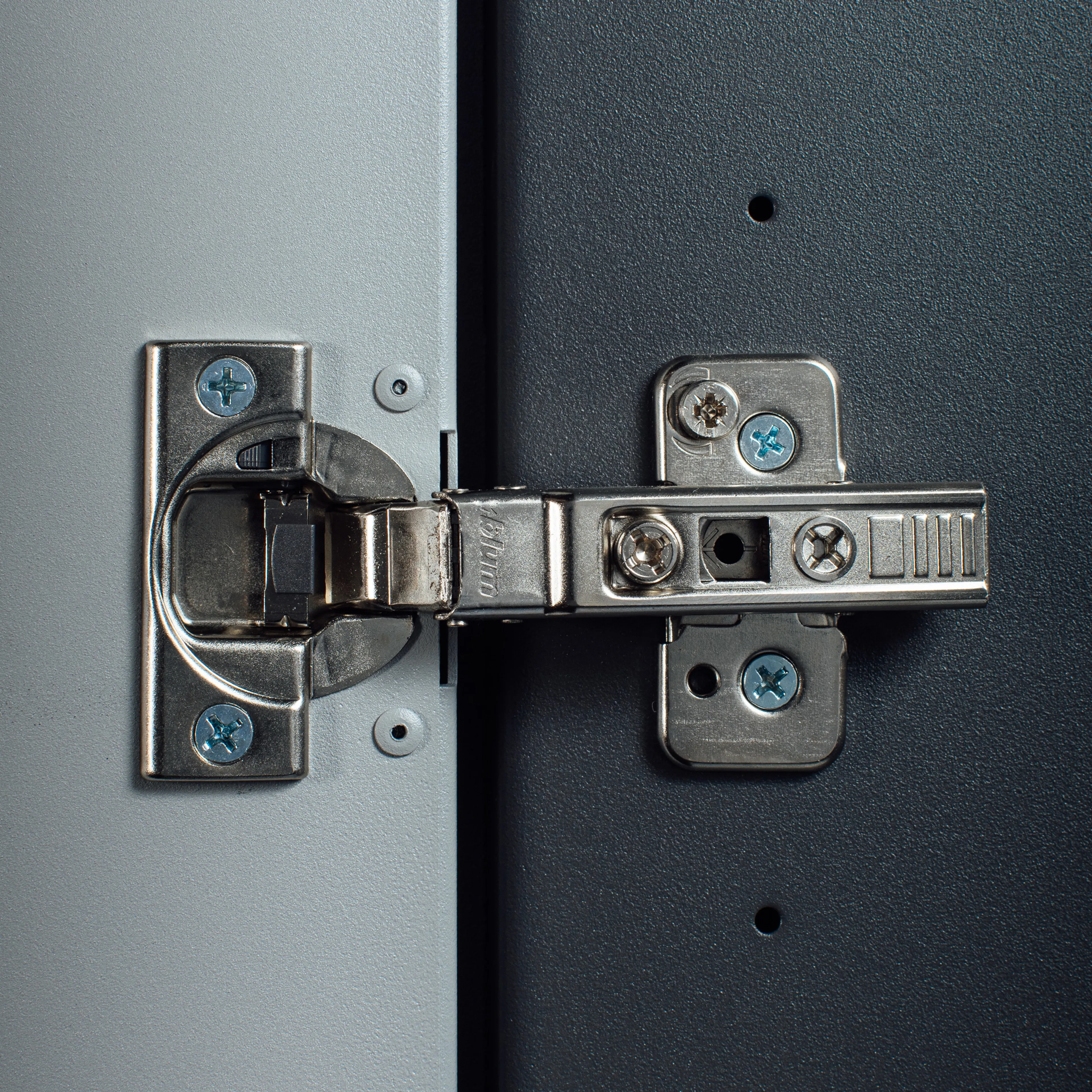 Close-up of a metal hinge showcasing meticulous craftsmanship, seamlessly joining two flat surfaces—one light gray and the other dark gray—with precision screws.