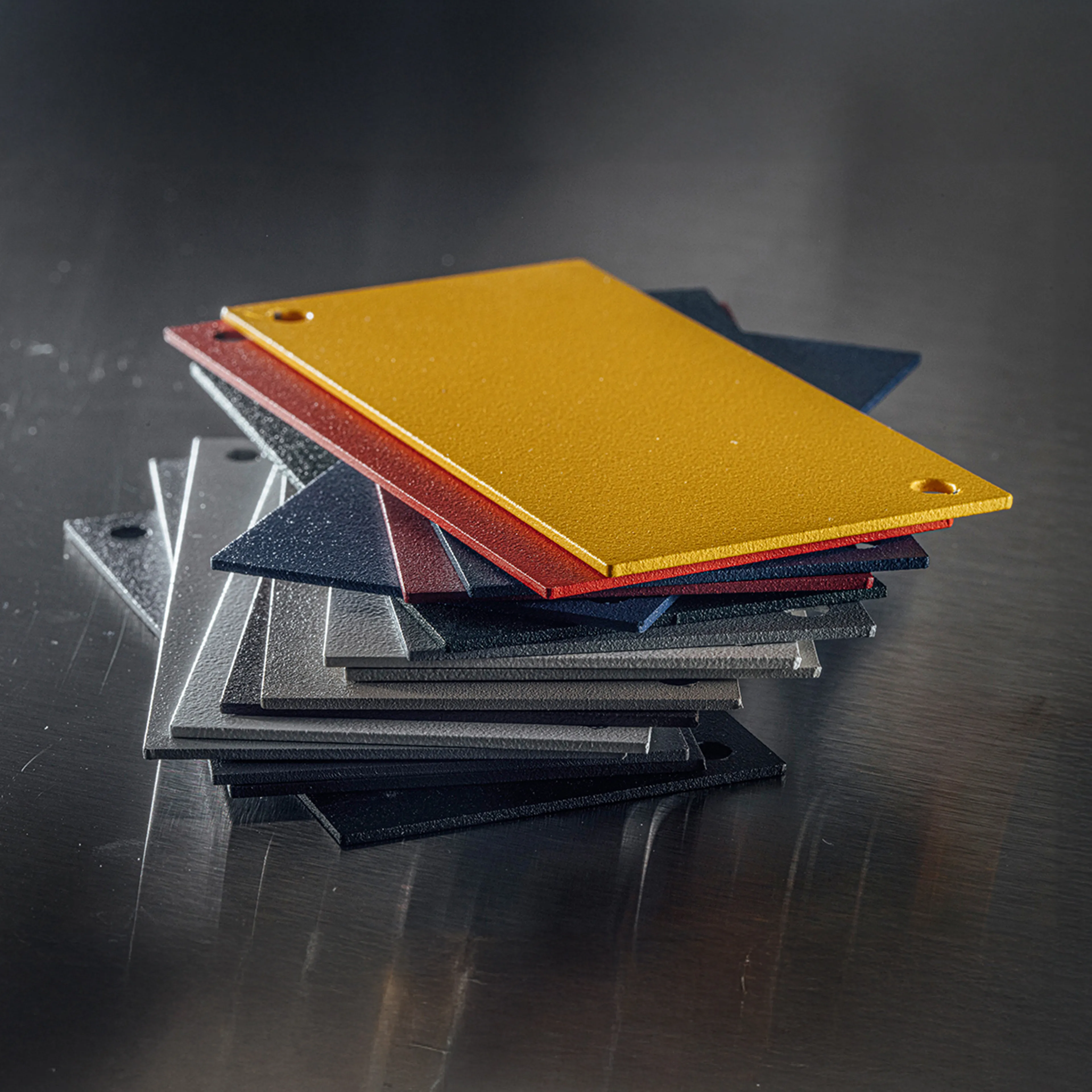 Stack of colorful metal sample sheets in yellow, red, blue, and gray, showcasing material options for cabinetry and design projects on a reflective surface.