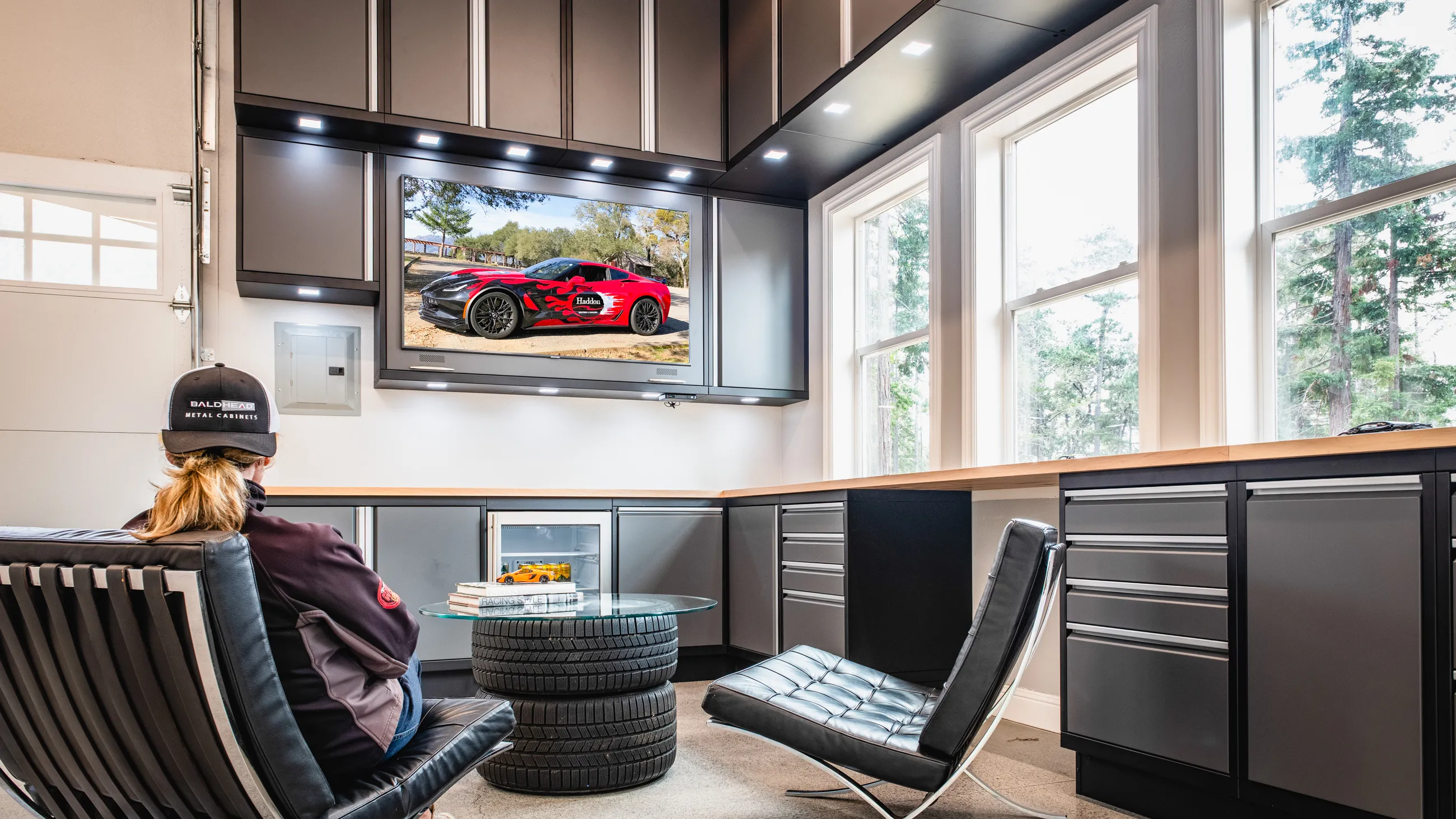 Modern luxury garage lounge featuring Baldhead Cabinets’ sleek matte gray metal cabinets, integrated storage solutions, and a custom workbench setup—combining high-end design with professional-grade functionality for automotive enthusiasts.