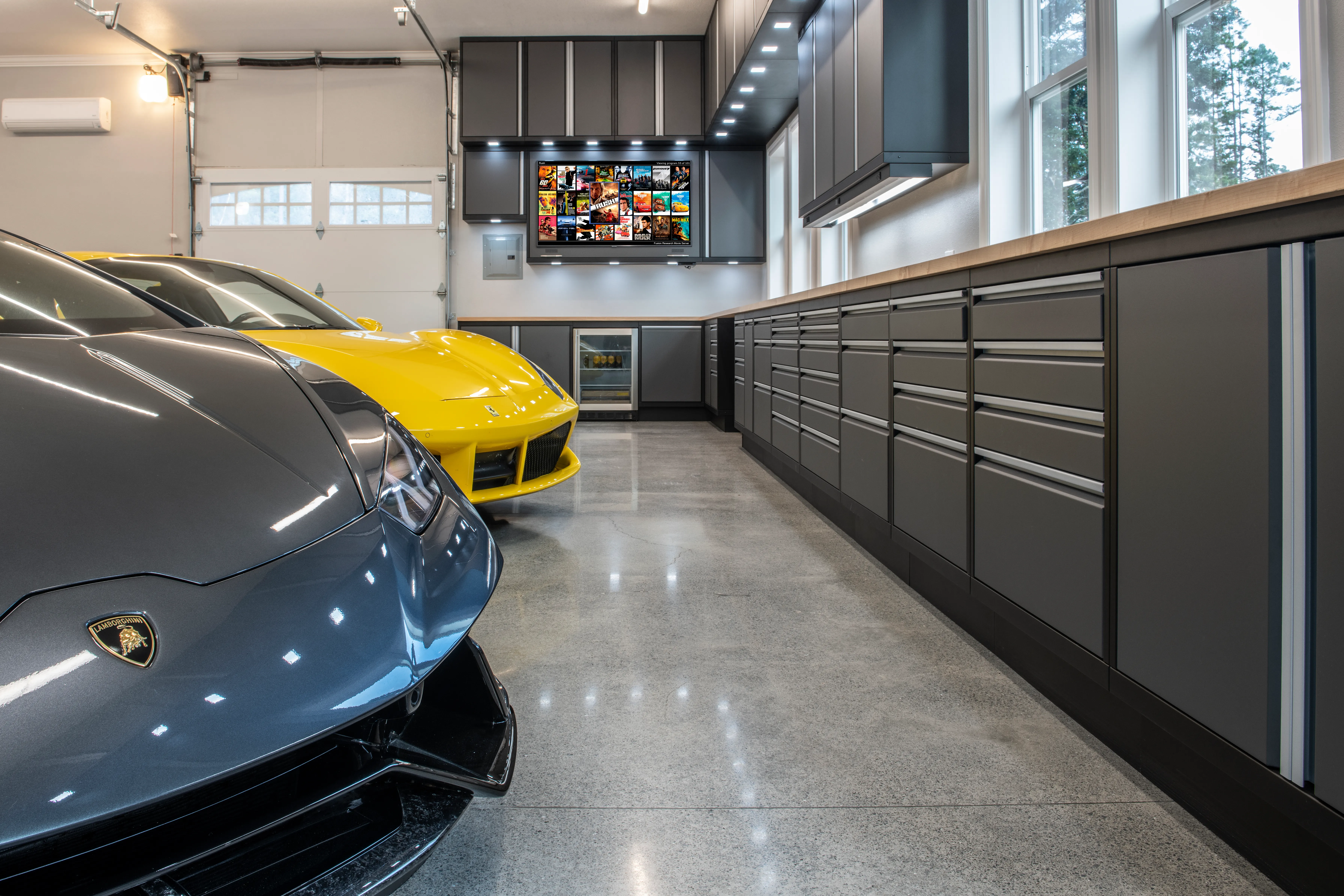 High-end garage featuring Baldhead Cabinets’ sleek gray metal cabinetry with integrated storage and butcher block countertops, showcased alongside luxury vehicles including a Lamborghini and Ferrari—ideal for premium garage organization and design.