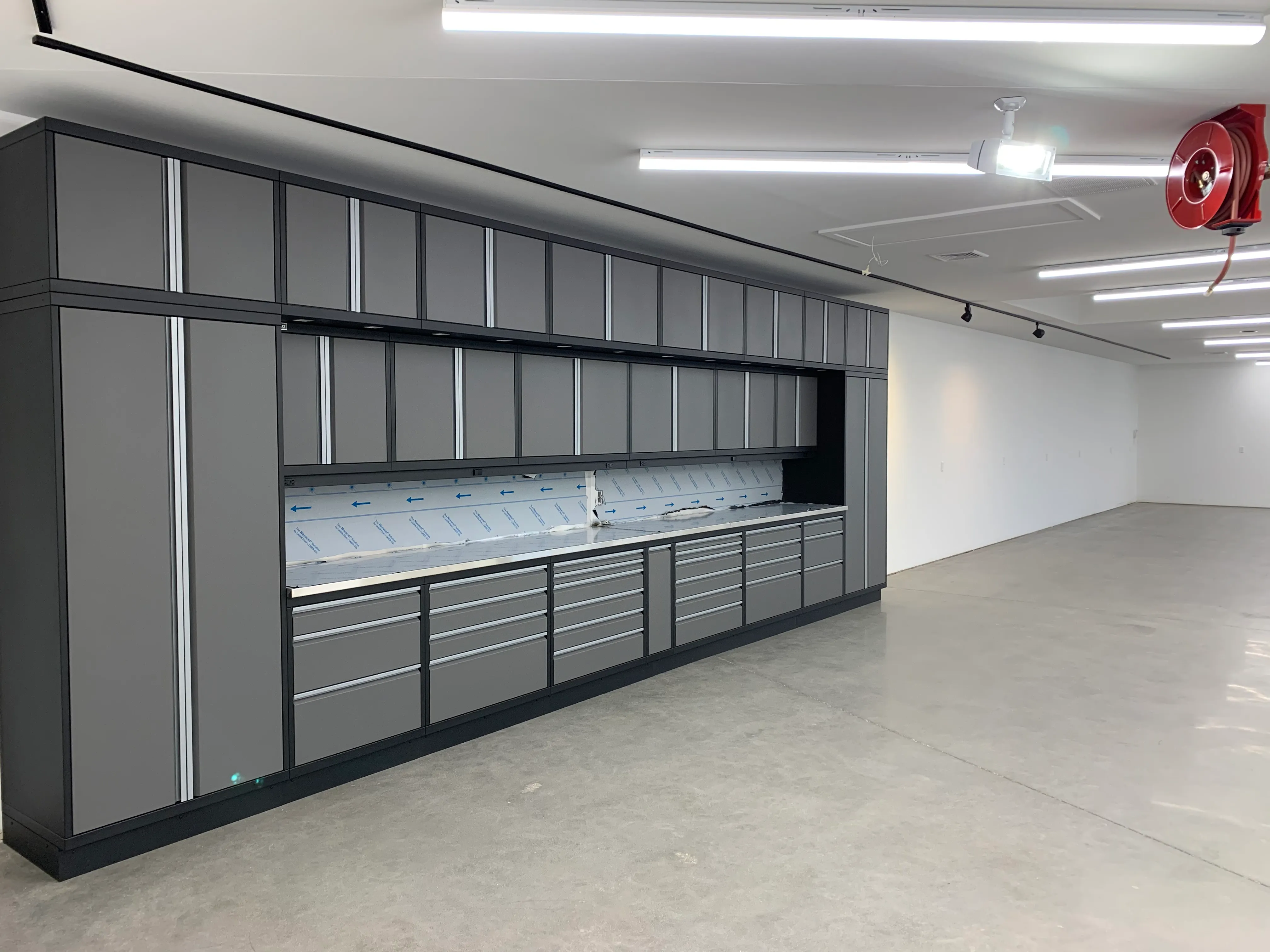 Sleek custom gray metal cabinet system by Baldhead Cabinets, featuring full-height storage, modular drawers, overhead compartments, and stainless steel countertops in a modern, high-end garage or workspace installation.