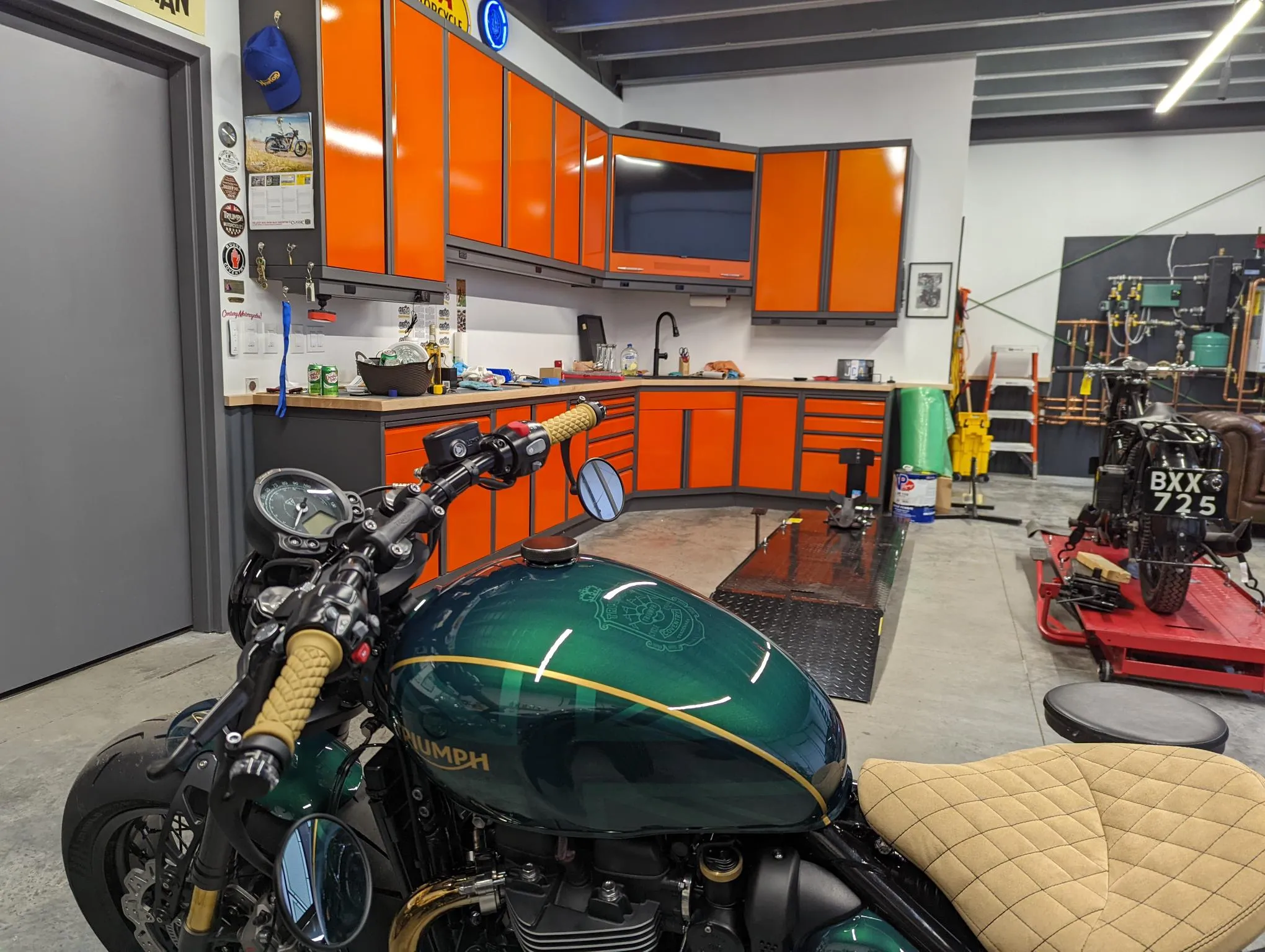 "Custom orange and black garage cabinets with integrated workspace, overhead storage, and built-in TV by Baldhead Cabinets — premium metal cabinetry for high-performance garages"