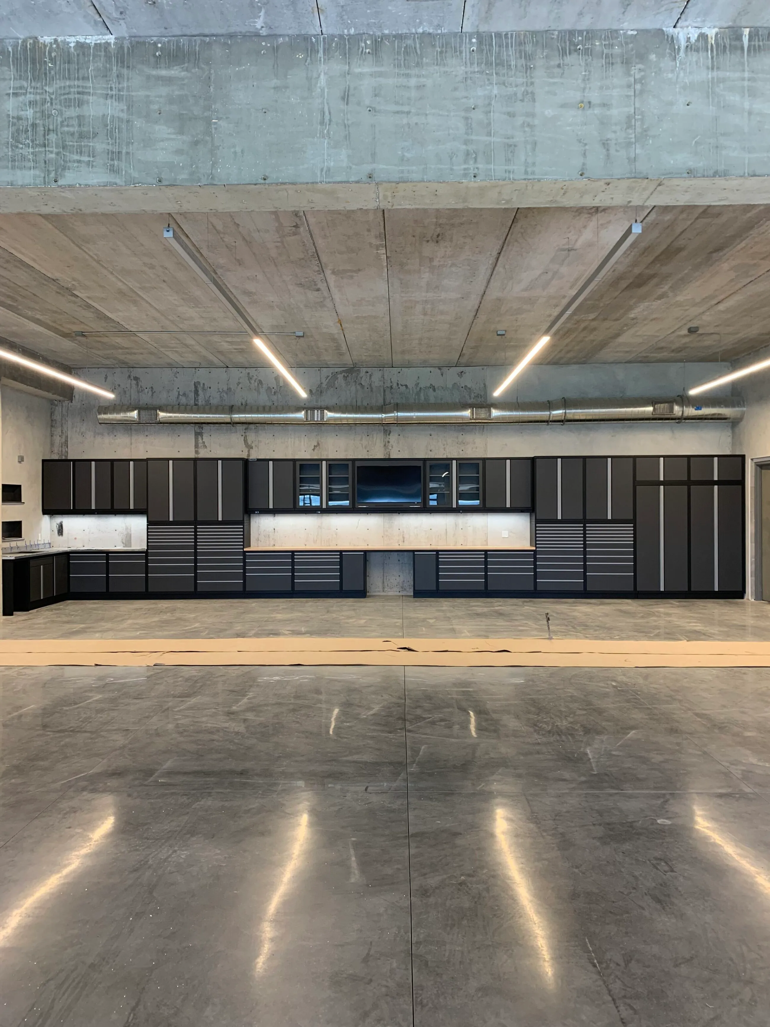 Expansive industrial garage featuring custom matte black Baldhead Cabinets with sleek silver trim, integrated workstation, and premium storage solutions. Ideal for high-performance garage organization and professional-grade functionality.