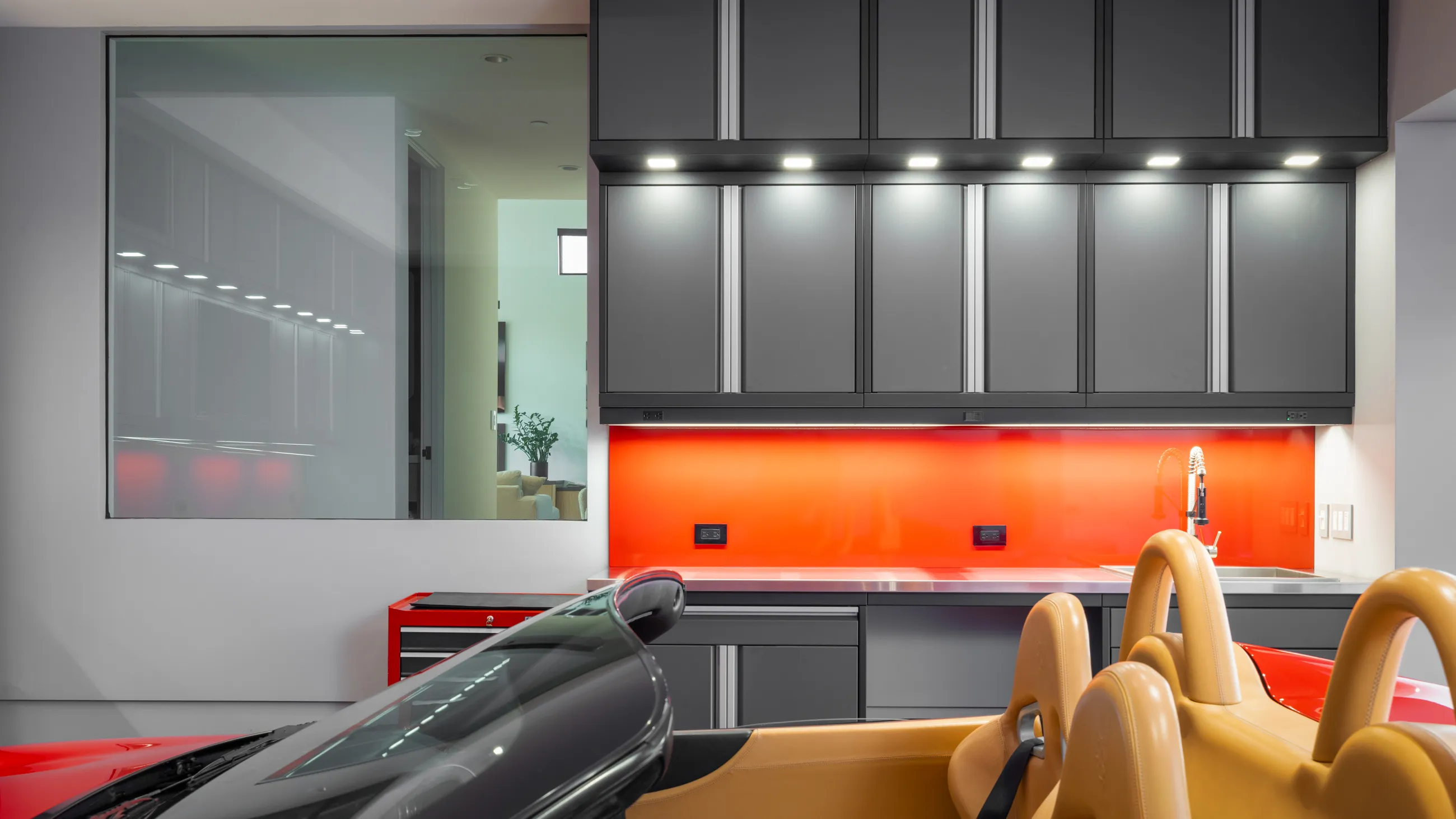 Premium garage workspace with custom matte gray Baldhead Cabinets, vibrant red backsplash, integrated sink, and luxury convertible sports car, showcasing a modern and functional garage design.