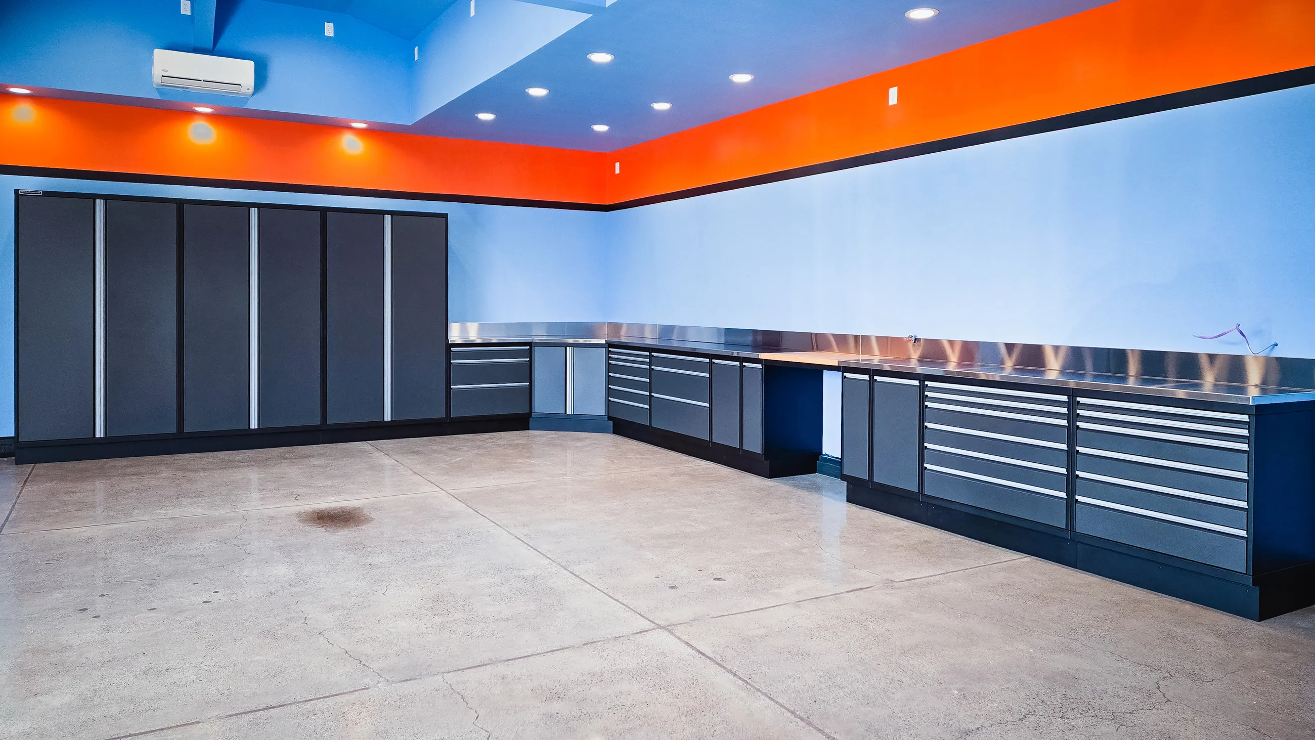Matte black and gray metal garage cabinets with full-length drawers and stainless steel countertops by Baldhead Cabinets — custom storage system for spacious garages with modern blue and orange interior design