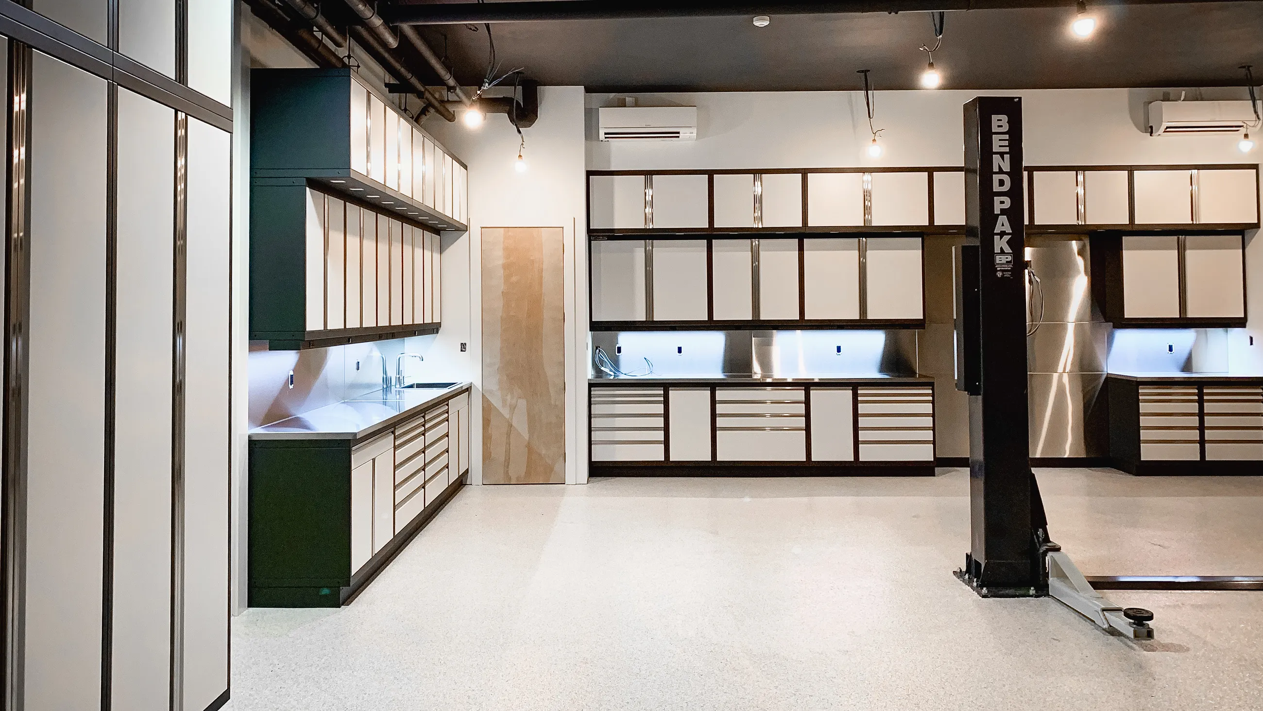 Luxury white and black garage cabinet system with stainless steel countertops, integrated sink, and under-cabinet lighting by Baldhead Cabinets — custom metal cabinetry designed for premium automotive garages and detailing shops