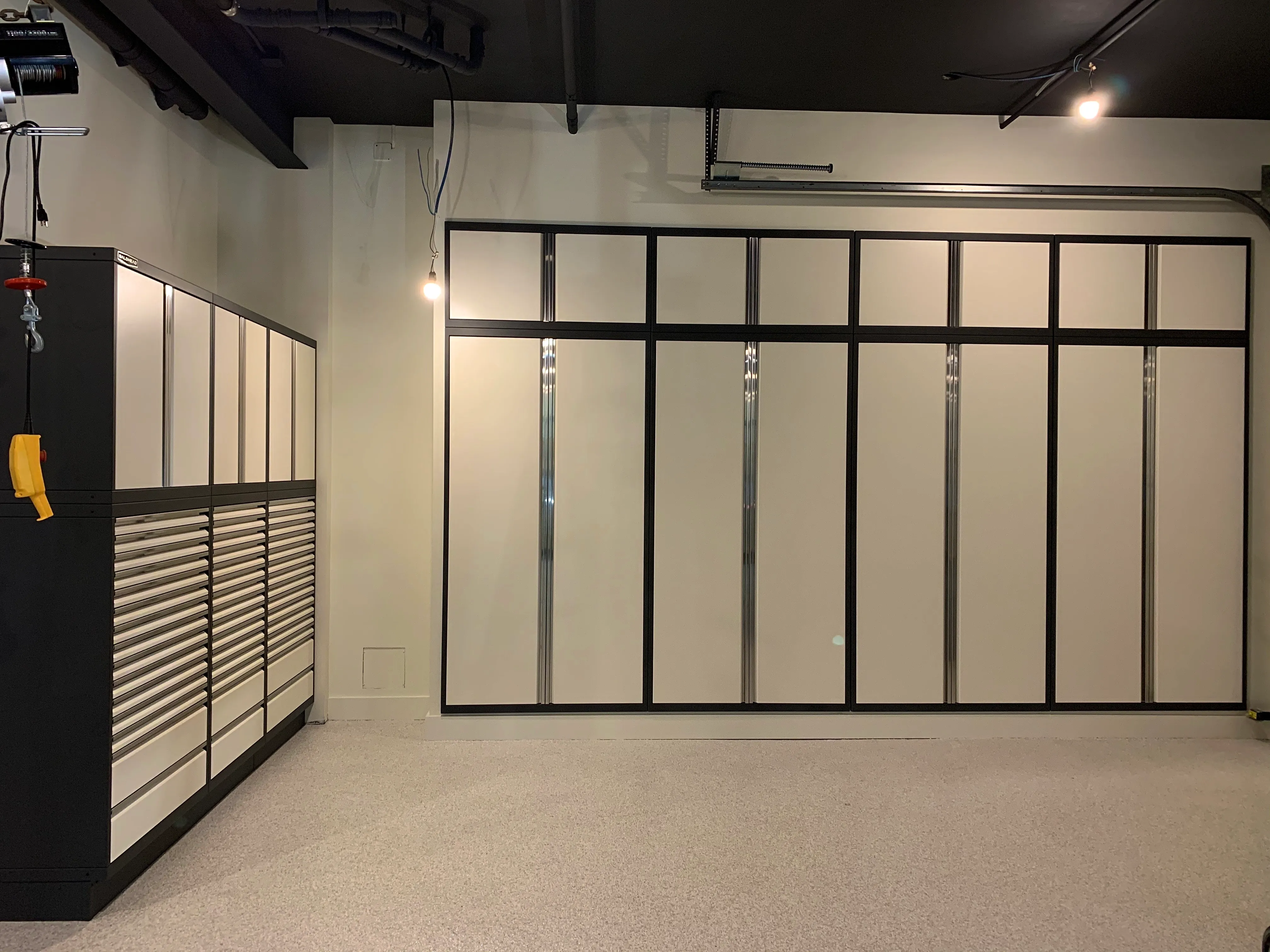 Custom two-tone garage cabinetry by Baldhead Cabinets featuring matte cream and black powder-coated finish, high-capacity drawers, full-height vertical storage, and clean epoxy flooring in a modern industrial workspace.
