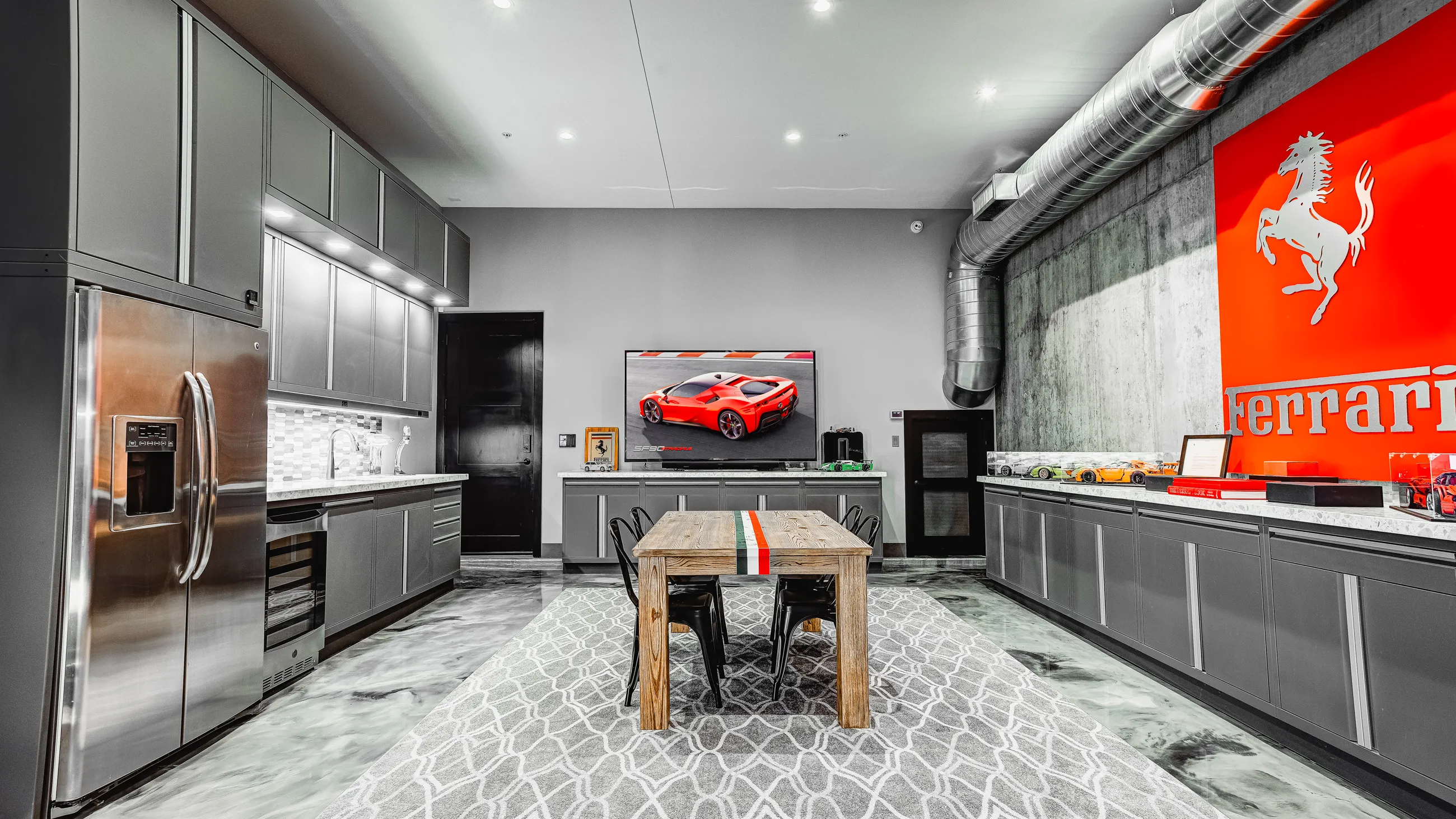 Luxury garage kitchen featuring custom Baldhead Cabinets in a sleek matte gray finish with integrated lighting. Showcasing a Ferrari-themed interior with high-end stainless steel appliances, a modern tile backsplash, and polished concrete floors. Ideal for automotive enthusiasts seeking premium garage cabinetry and designer workspaces.