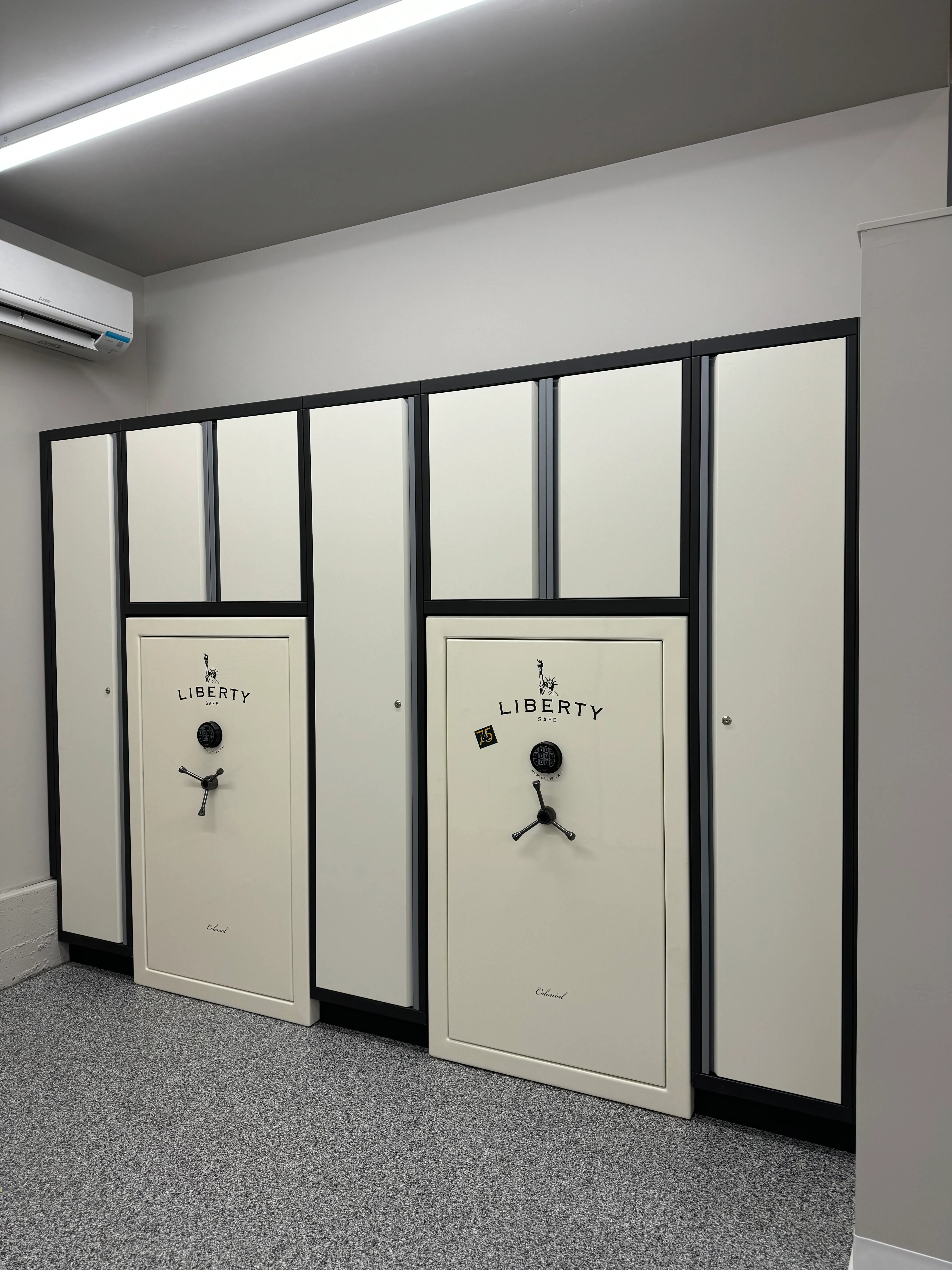 Custom-built Baldhead Cabinets with integrated Liberty gun safes, featuring a sleek black and cream powder-coated finish, flush design, and epoxy-coated flooring for secure, stylish storage in a climate-controlled garage space.