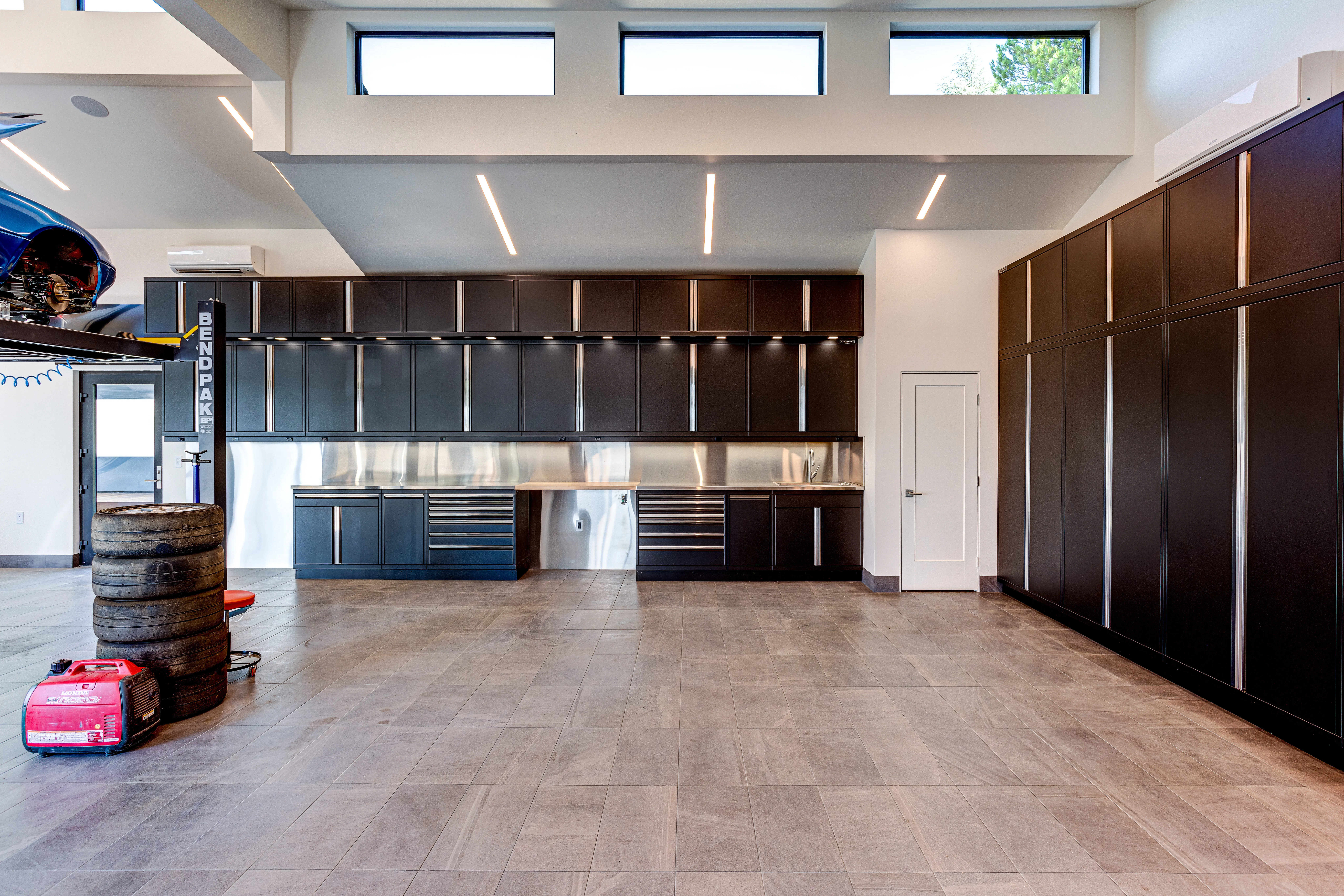 Sleek matte black garage cabinets with full wall storage, stainless steel countertops, and under-cabinet lighting by Baldhead Cabinets — custom metal cabinetry designed for luxury garage organization and professional-grade workspace functionality