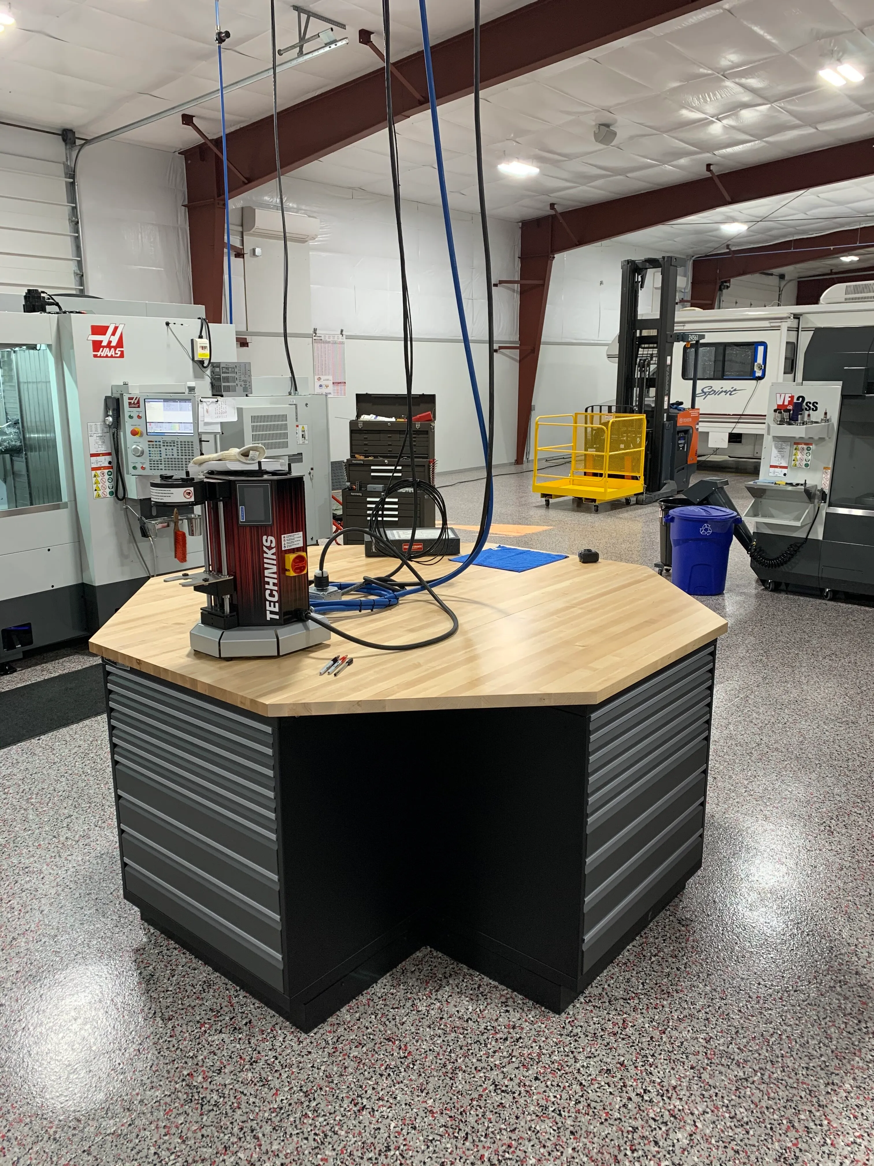 Custom industrial tool station by Baldhead Cabinets featuring a hexagonal butcher block work surface, integrated heavy-duty drawers, and ergonomic cable management in a high-performance CNC machining facility with epoxy flake flooring.
