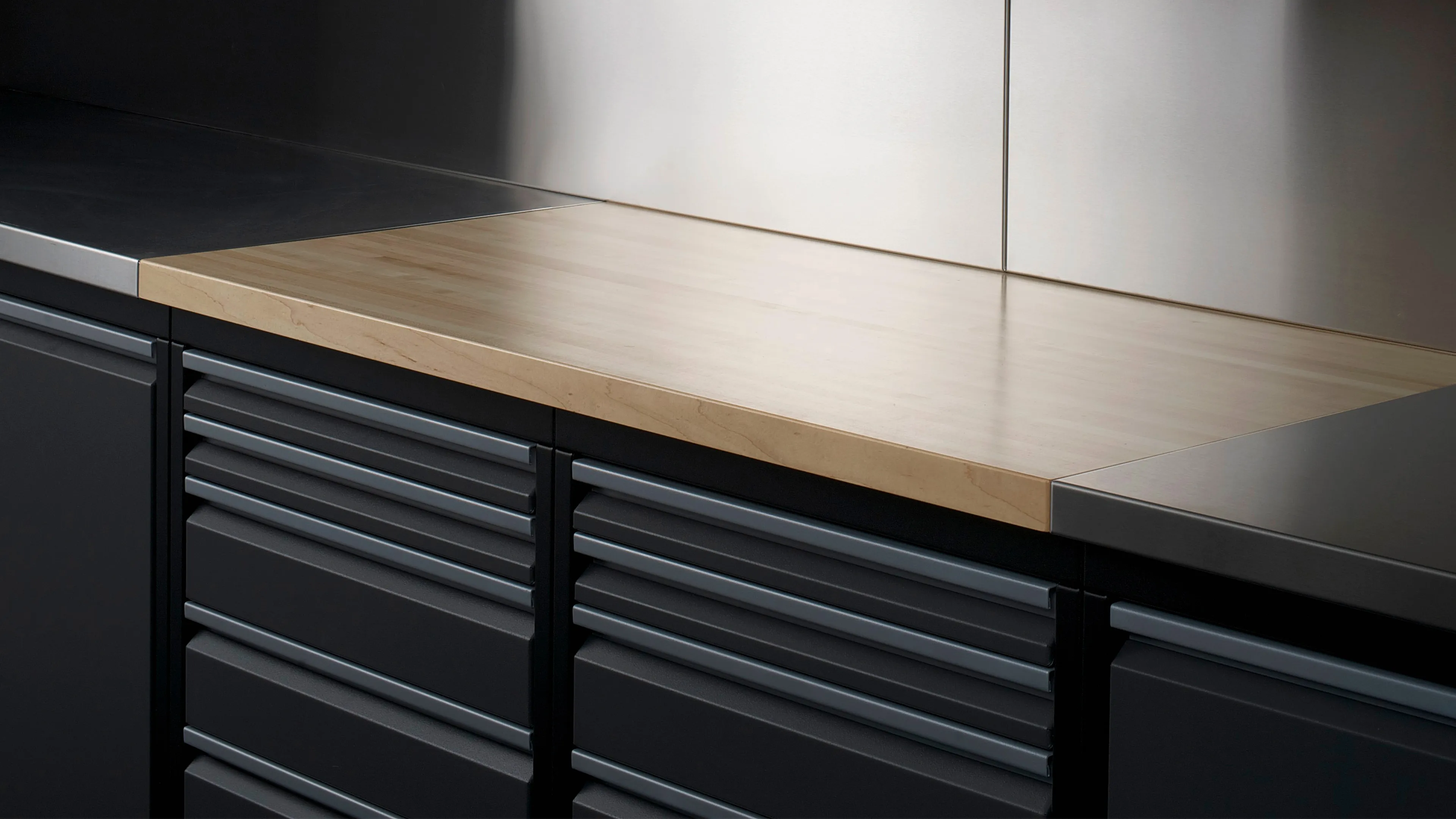 A clean wooden countertop with adjacent dark cabinets and a metallic backsplash, featuring multiple drawers for optimal storage solutions.
