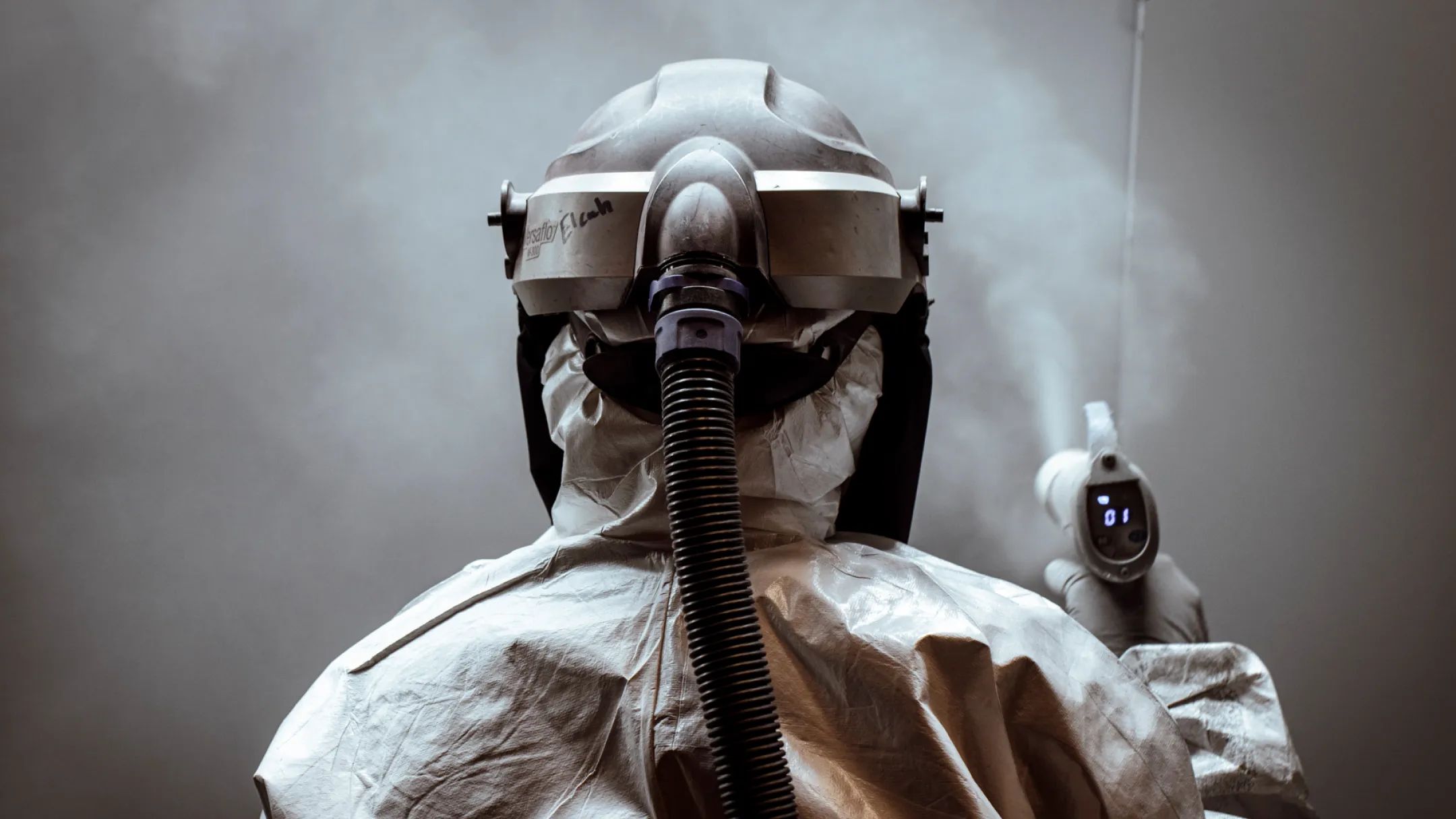 A worker in protective gear uses a device in a misty environment, ensuring safety standards at Baldhead Cabinets.