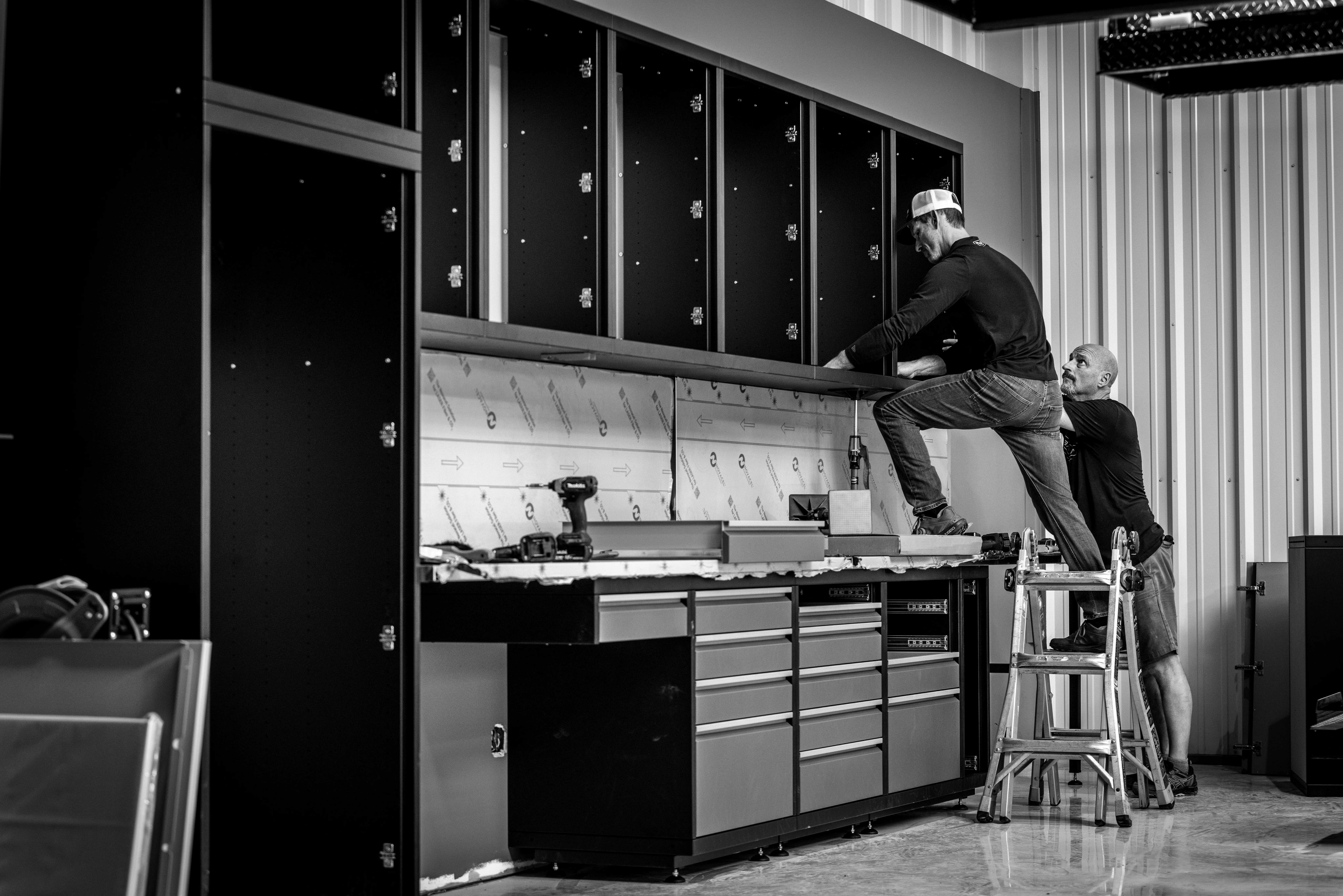 A person in protective gear meticulously operating a spray gun in a controlled environment, involved in the manufacture of custom metal cabinets. The scene emphasizes the process of creating high-quality cabinets for tools, showcasing precision and care in the production.