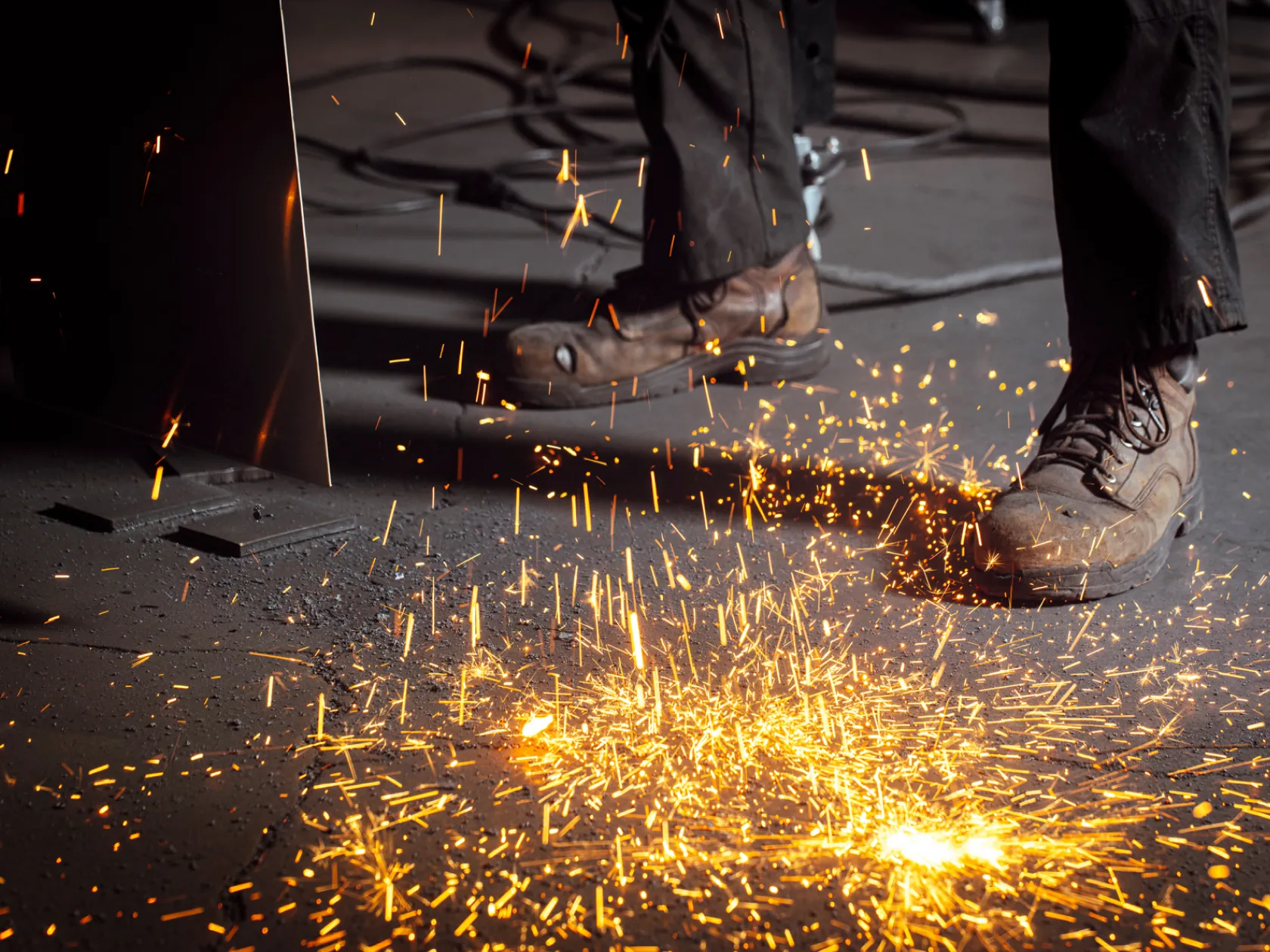 Close-up of worker's boots with sparks flying during metal cutting or welding at Baldhead Cabinets.